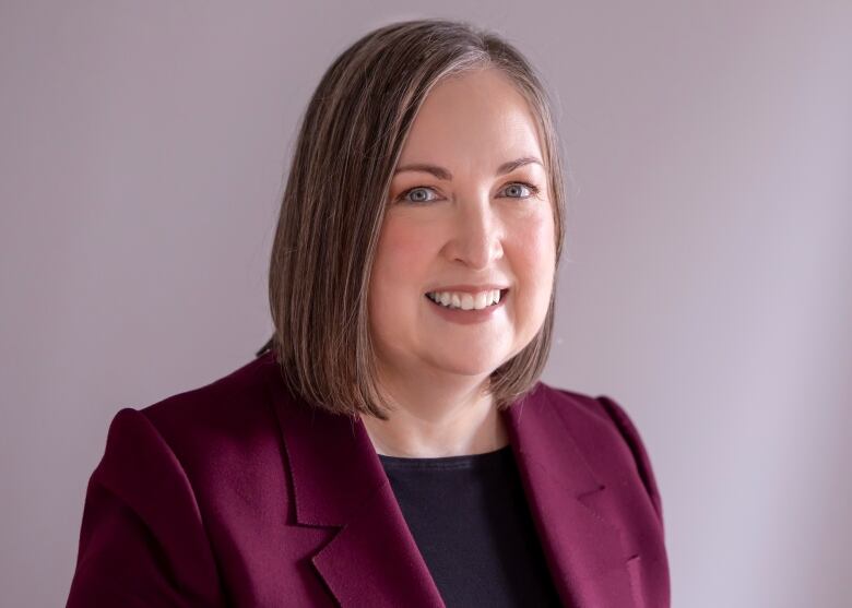 Woman with chin-length brown hair wearing burgundy blazer with black top.