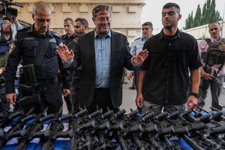 Men stand in front of a table piled with automatic weapons.