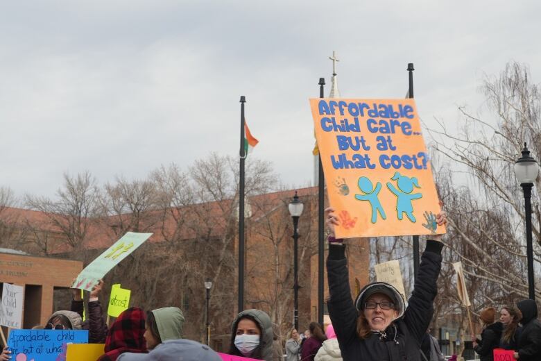 a woman stands in front of a crowd and holds a sign that says 