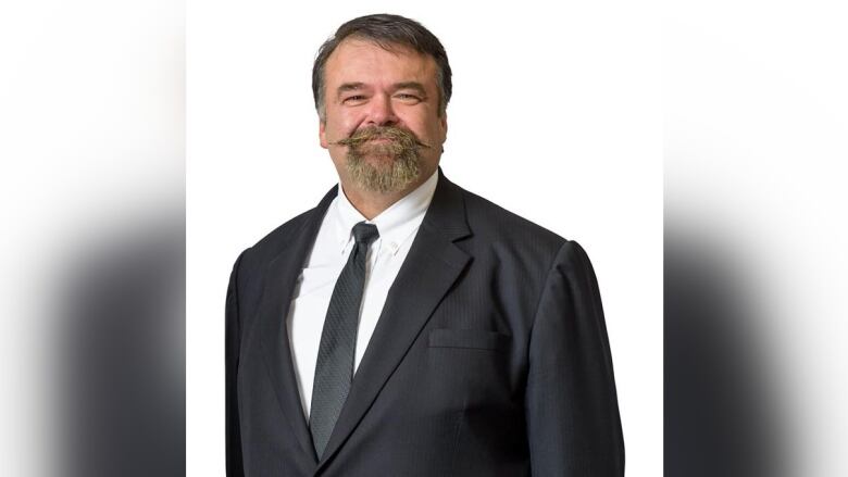 MLA Greg Lawrence is depicted, a man with a beard and mustache wearing a suit and tie.