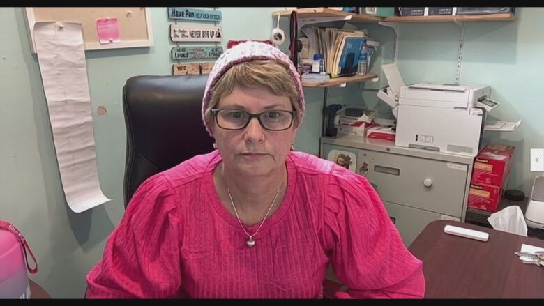 Woman with pink shirt and hat sitting in office.