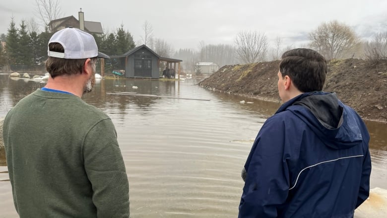 A farmer stands and looks over a flooded farm field on a rainy day.