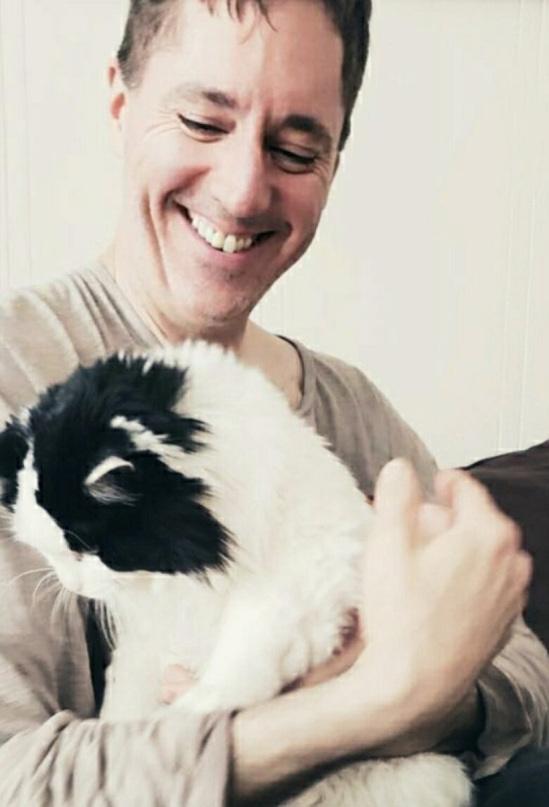 A smiling man looks down at a black-and-white cat he's holding in his arms.