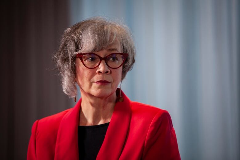 A woman in a red coat and a winged pair of glasses is pictured during a news conference.