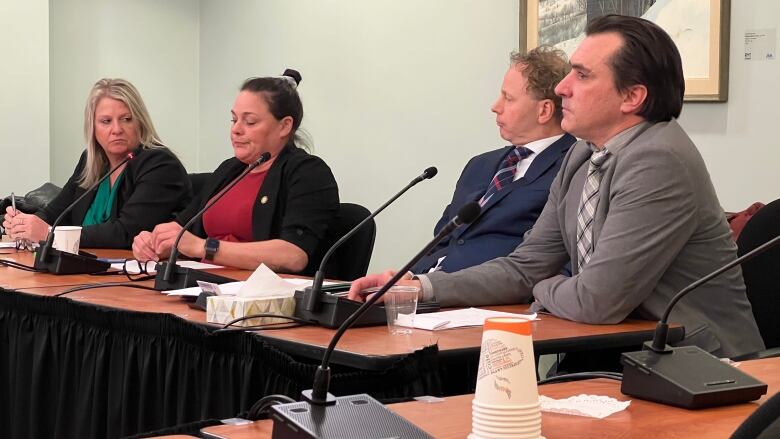 four people in business attire sit at a table with microphones