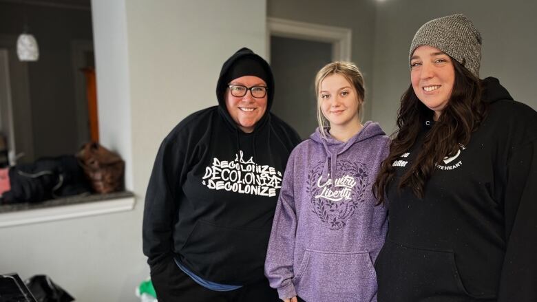 Three young women wearing hoodies and sweatpants smile at the camera.