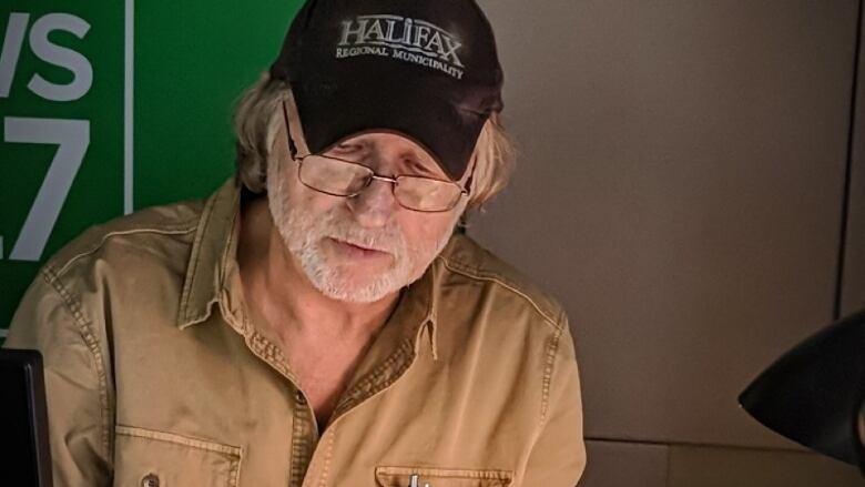 A man in a collared shirt and black baseball cap looks down as if reading.