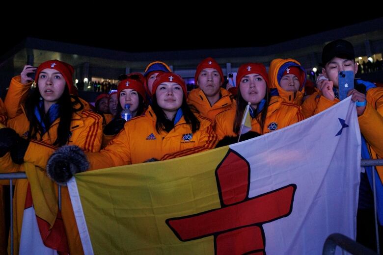 A group of young people in matching yellow jackets hold up a Nunavut flag.