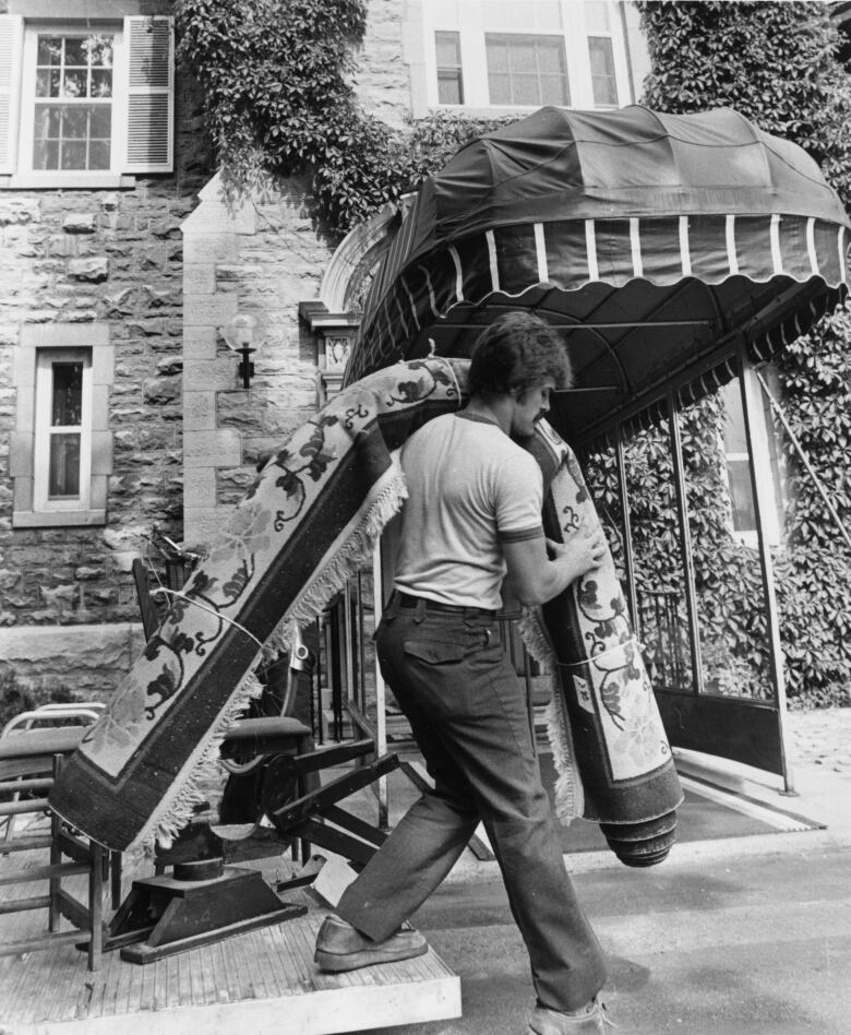 A man carries a carpet into a house.