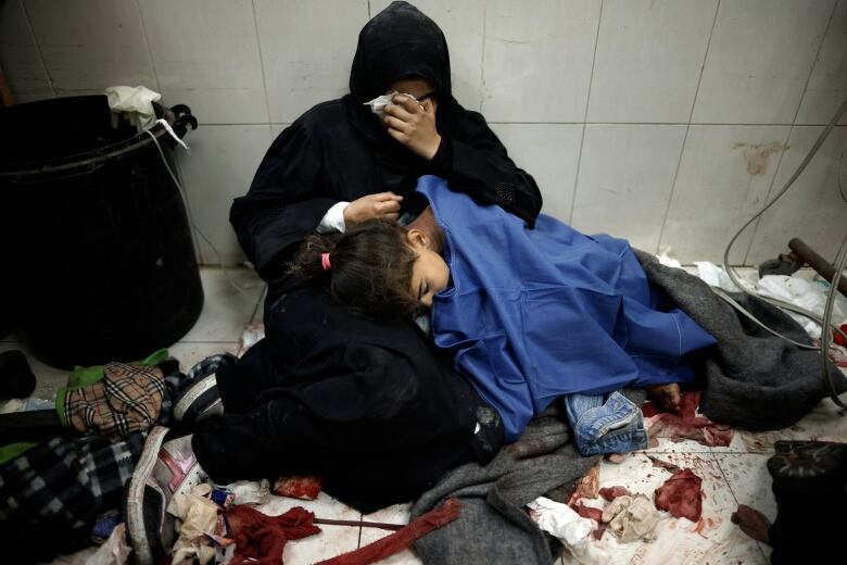 A woman in black cradles a wounded child on the floor of a hospital.