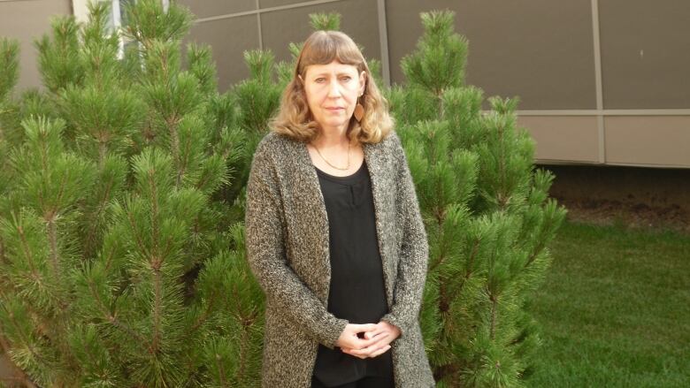 A woman stands by a green bush.