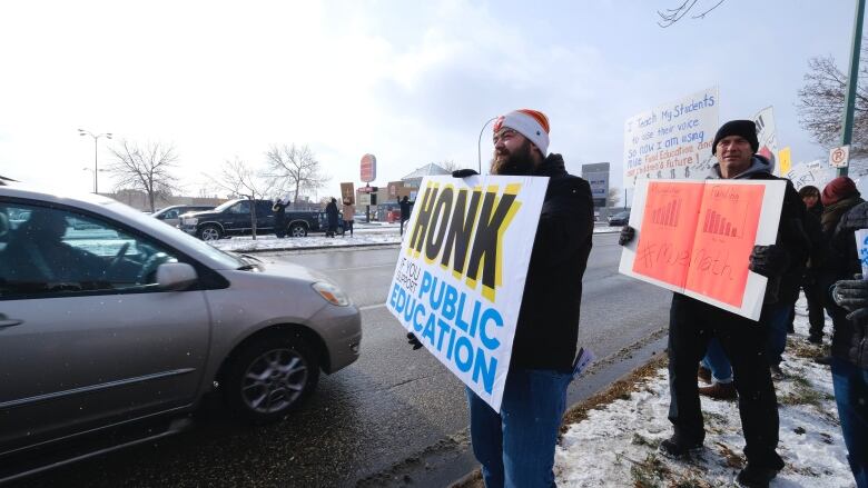 A person in winter gear is holding a sign that reads honk for public education.