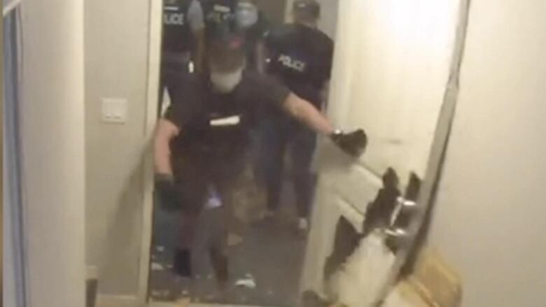 Police enter an apartment unit and push open a broken door.