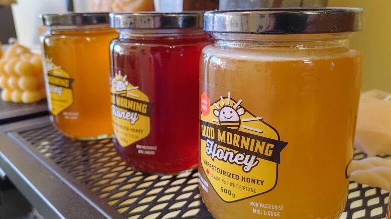 Three glass jars filled with honey sit in a line on a shelf.