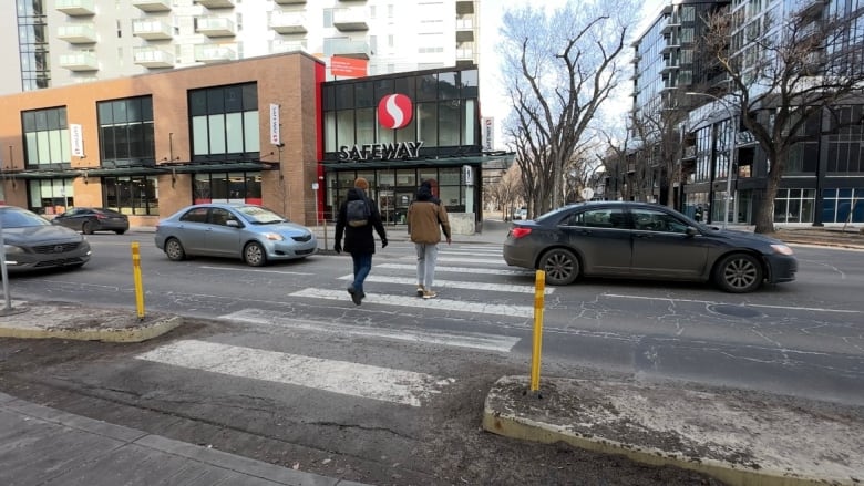 Two people wearing winter jackers crossing a road with cars driving by.