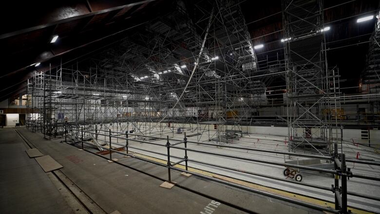 Inside a vast building, a pool that's empty and filled with scaffolding.