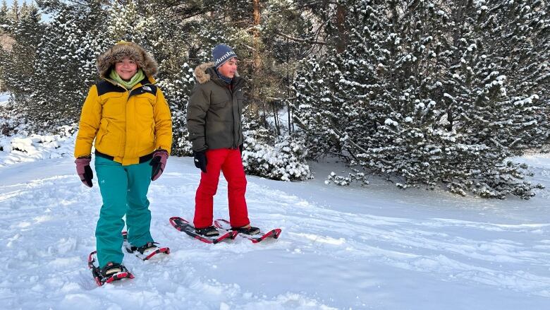 A woman and a boy snowshoe side by side while wearing full winter gear.