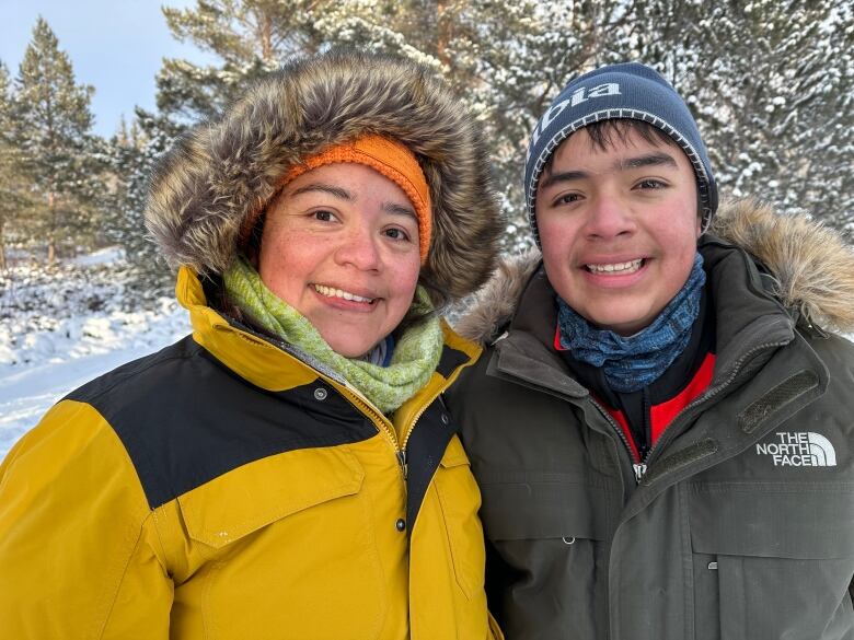 A woman and a boy pose for a photograph outside in full winter gear.