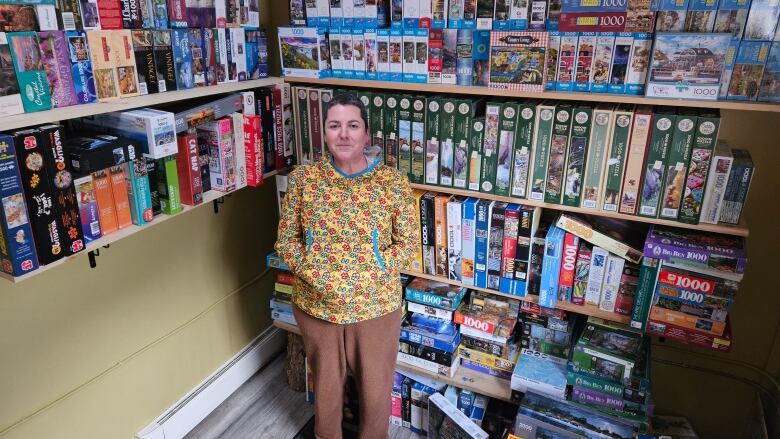 A woman stands in front of a huge shelf of puzzle boxes