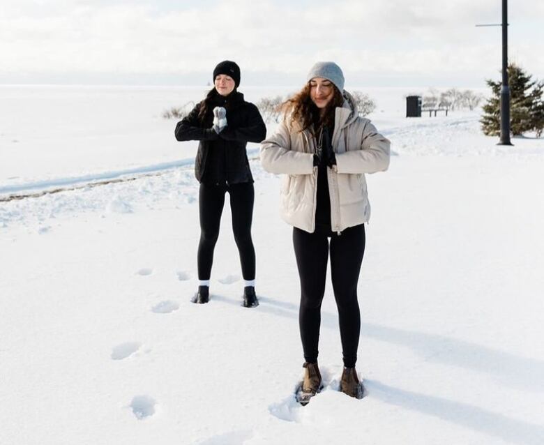 Two women doing yoga in the snow. 