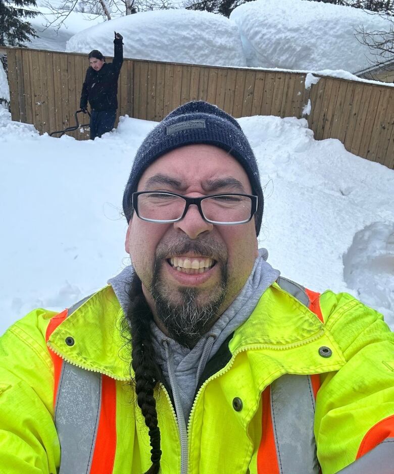 An Indigenous man in a yellow safety jacket helps clear snow