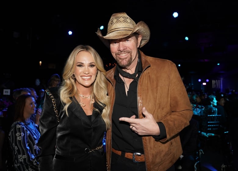 A man in a cowboy hat and a light-haired woman smile while posing for a photo.