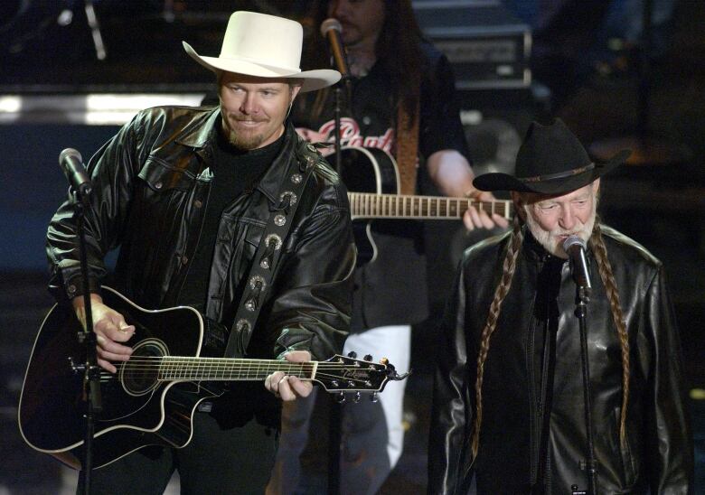 Two bearded men in cowboy hats, one older and one younger, are shown performing on stage