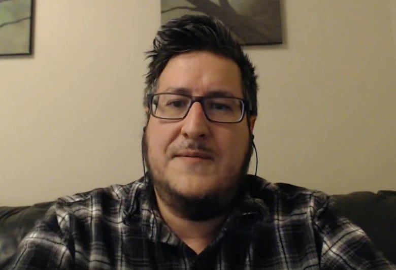 Jonathan Jenka in front of a plain background, wearing a plaid shirt.