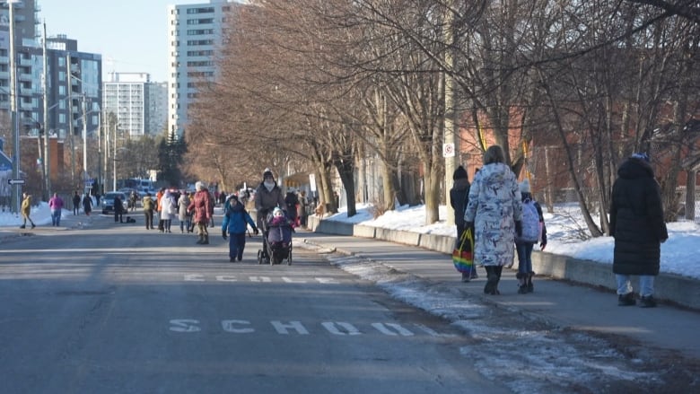 Parents and children walk to school on a closed residential street in winter.