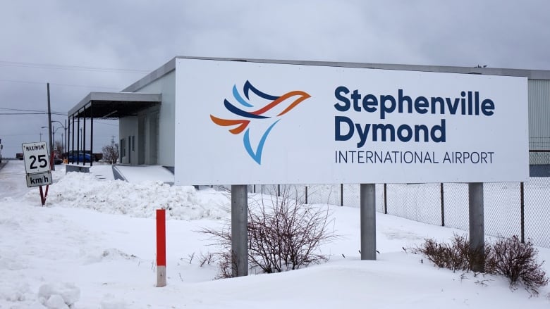 A sign stands in front of a building and an airport.