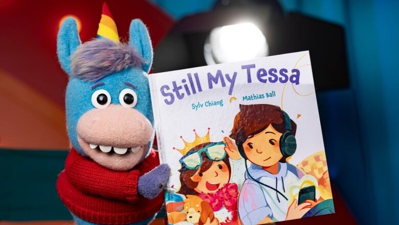 A unicorn puppet holds up a picture book to the camera.