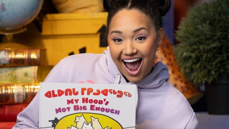 A woman holds a picture book up to the camera and is smiling. 