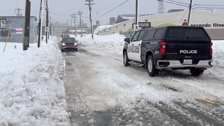 A black-and-white sport utility vehicle with police on the door drives down an icy street with large snowbanks on either side.