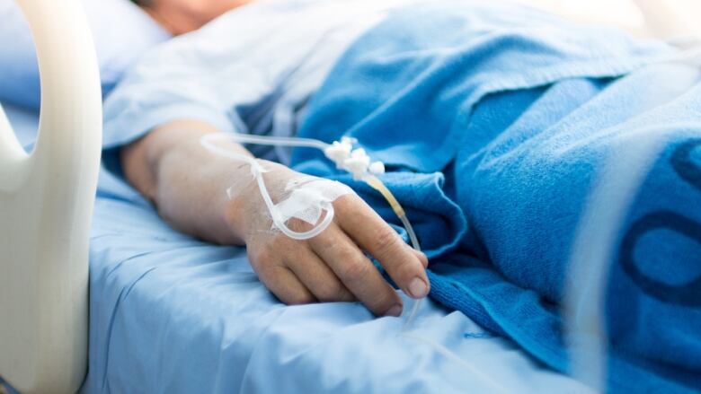 A patient's hand sits on top of a blue hospital blanket, with an IV tube inserted.