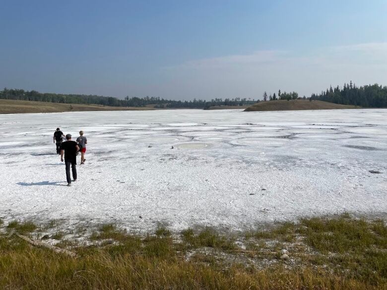 Three people are pictured walking on a salt flat. 