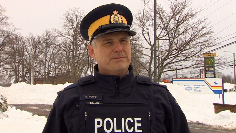 A man with grey hair wears a police uniform while standing in front of a snow bank. 