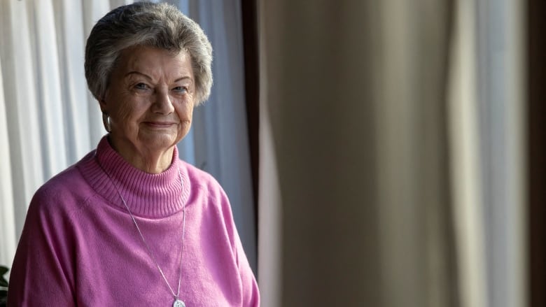 An older woman in a blouse smiles while posing for a photo indoors.