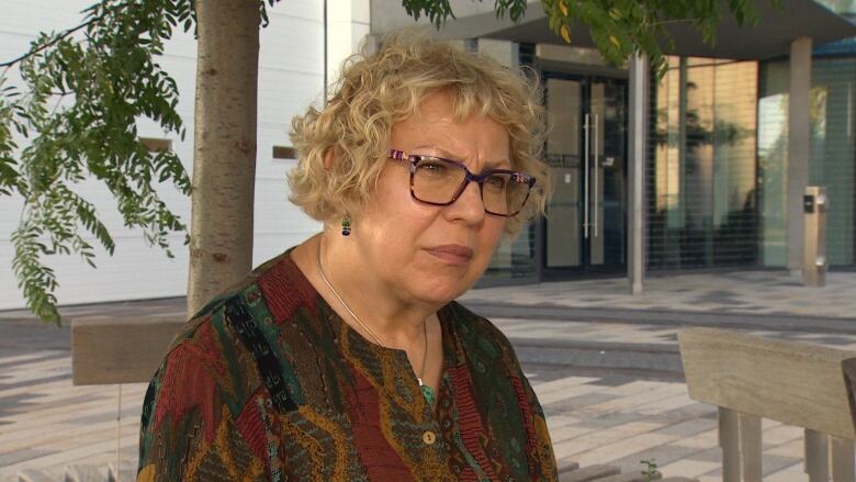 A woman wearing a patterned shirt and glasses sitting in a lobby. 