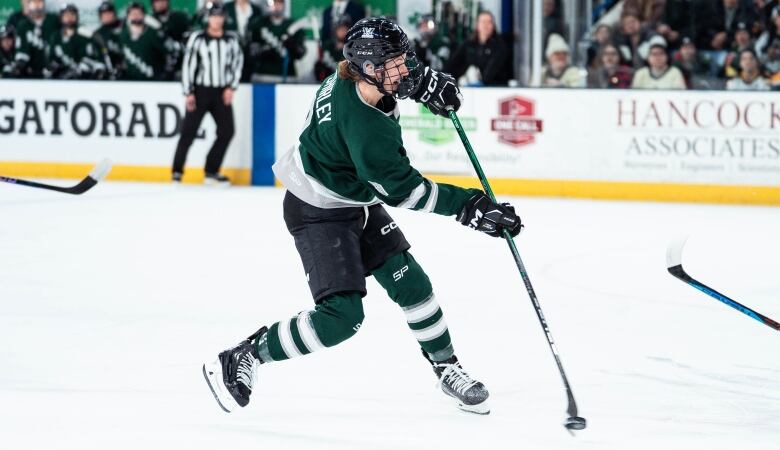 A hockey player in a green Boston jersey takes a shot on the ice.