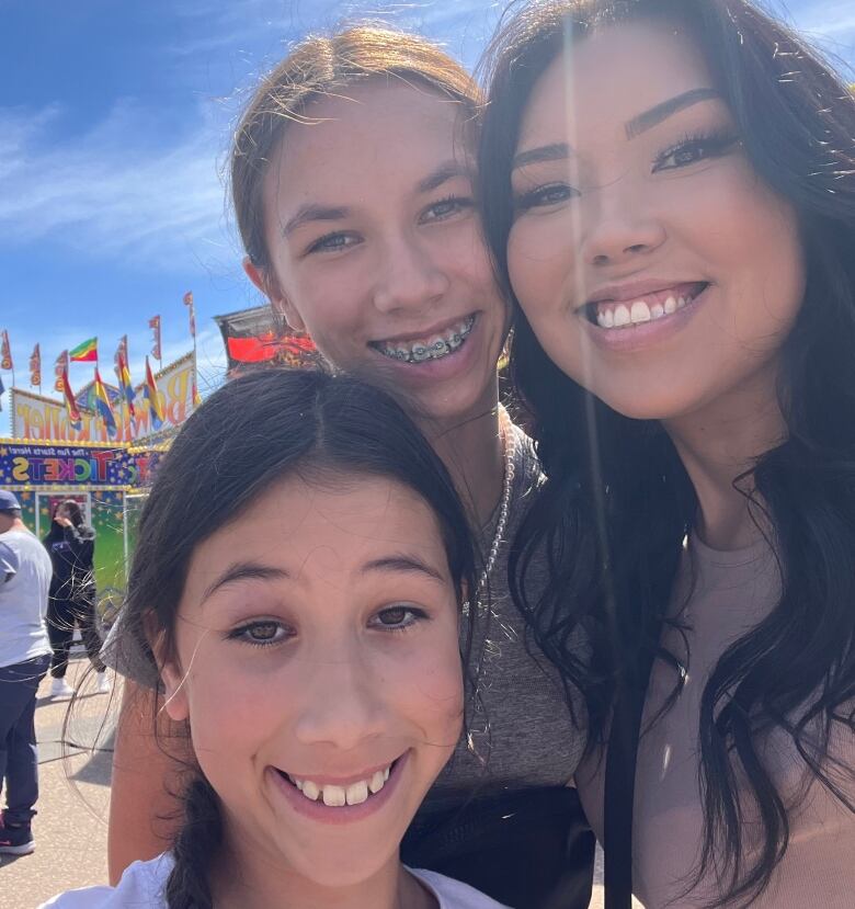 A head-shot / selfie of a woman and two younger girls with blue sky in the background.