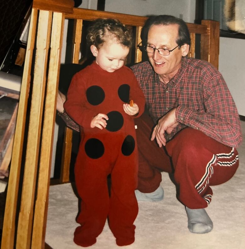 A man in red sweat pants and a red plaid shirt crouches next to a child. 