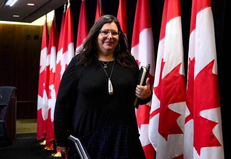 A woman wearing black walks in front of Canadian flags.