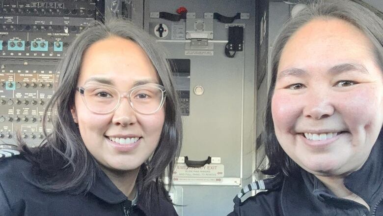 Two women smile and take a selfie in the cockpit of an aircraft