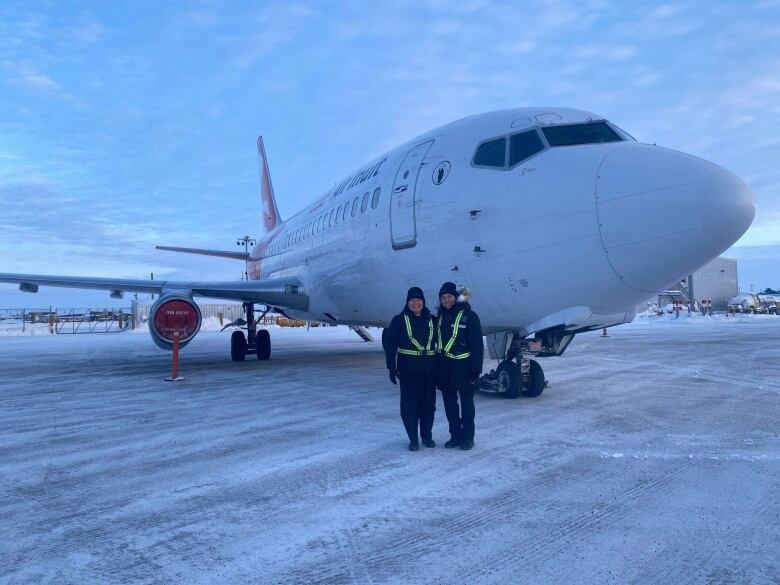 Two people stand on the tarmac outside of an airplane