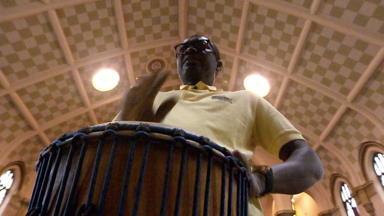 A man in a yellow shirt plays the drum 