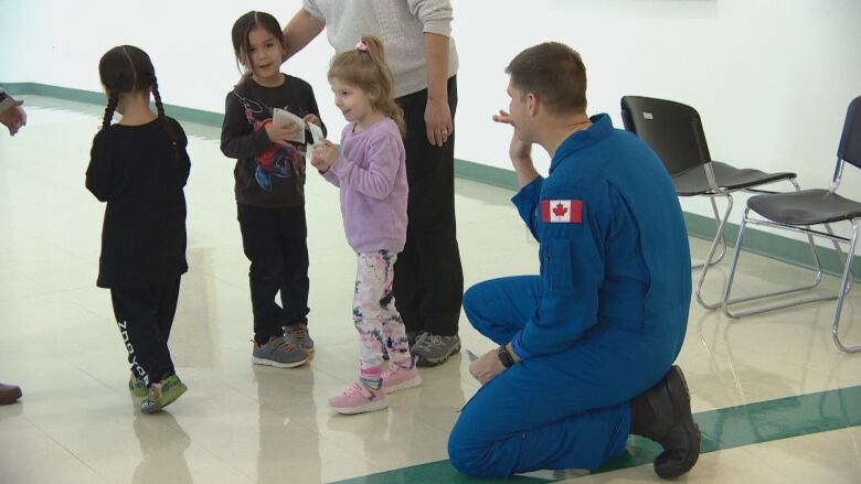 Three kids stand to the left of Hansen, while he kneels down to wave at them.