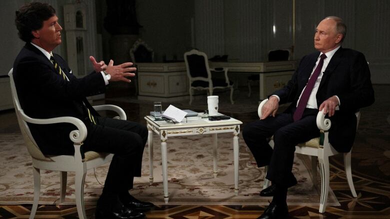 Both seated, U.S. TV host Tucker Carlson interviews Russian President Vladimir Putin.