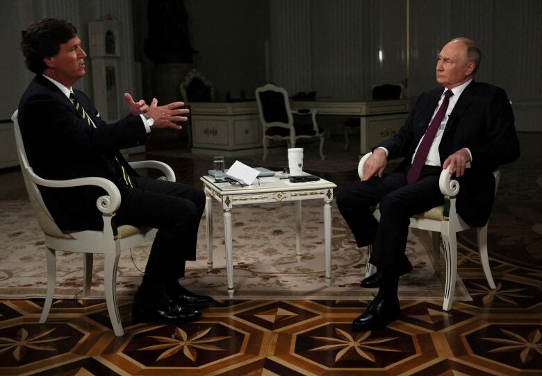 Both seated, U.S. TV host Tucker Carlson interviews Russian President Vladimir Putin.