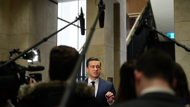 A politician talks to a scrum of reporters in a legislature lobby.