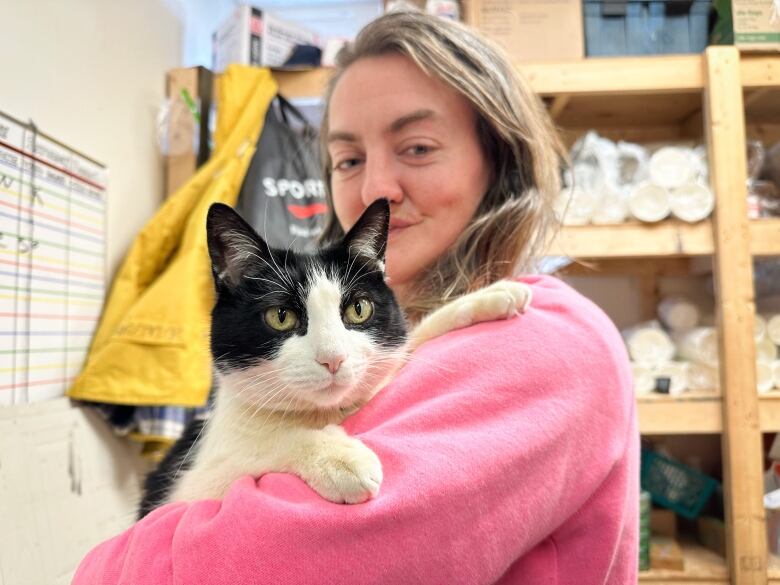 A woman with long light-coloured hair and a pink sweater holds a black-and-white cat 